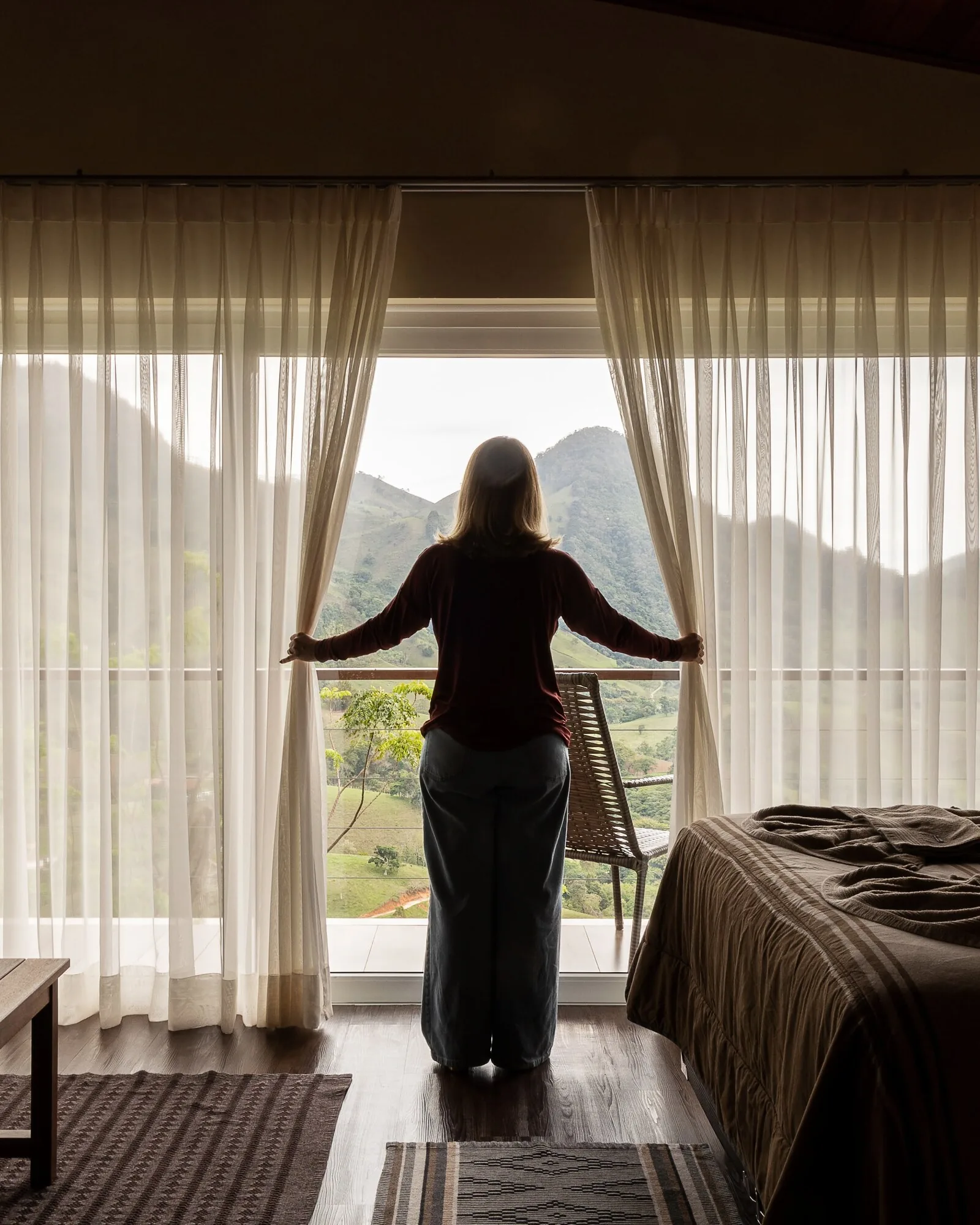 Quarto do chalé com cortinas leves abertas para a vista das montanhas pela manhã